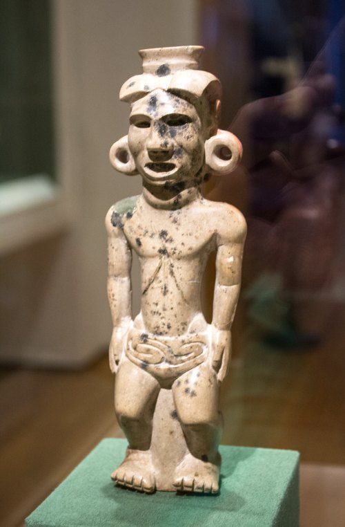 A small, ancient figurine with distinct facial features and large ear ornaments, displayed on a green pedestal.