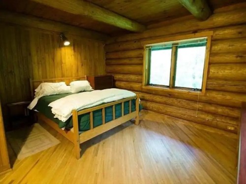 Cozy log cabin bedroom with a wooden bed, green bedding, and large windows letting in natural light.