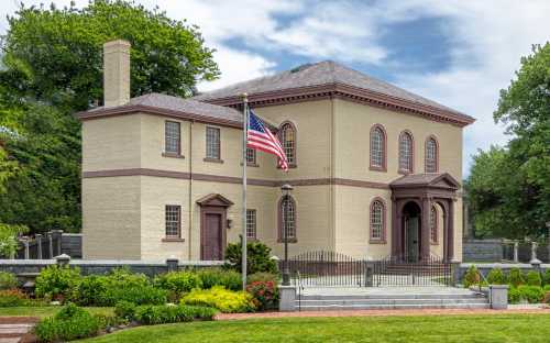 Historic building with a flag, surrounded by greenery and a decorative fence, under a cloudy sky.