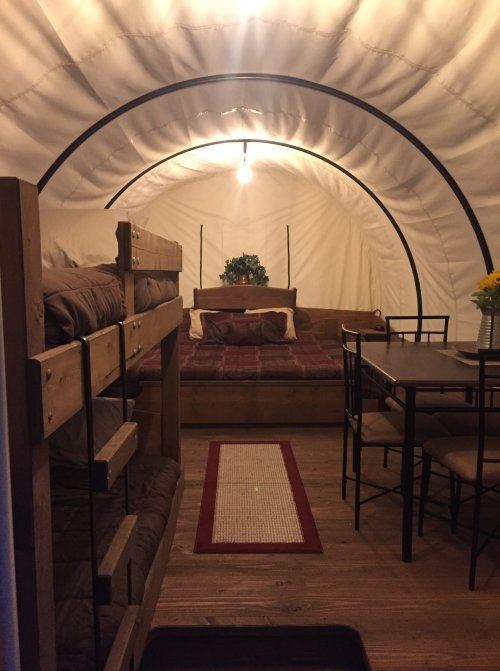 Cozy interior of a glamping tent featuring bunk beds, a double bed, dining table, and warm lighting.