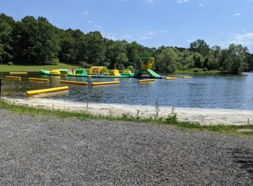A colorful inflatable water park on a lake, surrounded by green trees and a sandy beach.