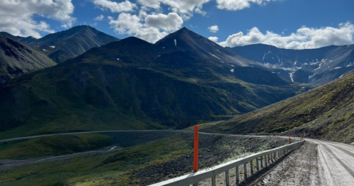 A winding road through a mountainous landscape under a blue sky with scattered clouds.
