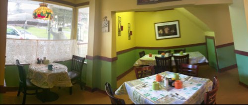 Cozy restaurant interior with tables set for dining, colorful decor, and a large window letting in natural light.