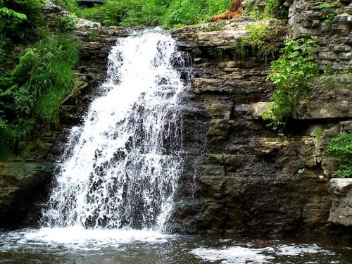 A small waterfall cascading over rocky terrain, surrounded by lush green foliage.