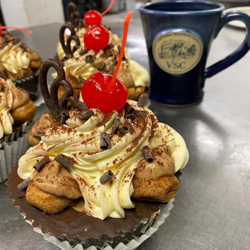 Delicious cupcakes topped with chocolate frosting, cherries, and chocolate shavings, alongside a blue mug.