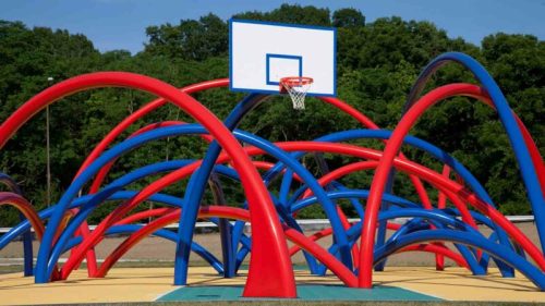 Colorful, abstract basketball court with red and blue arches and a hoop against a green tree backdrop.