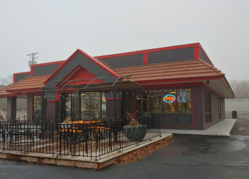 A red and black fast-food restaurant with an "OPEN" sign, featuring outdoor seating and a foggy background.