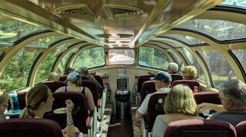 Interior view of a scenic train car with passengers enjoying snacks while traveling through a lush landscape.