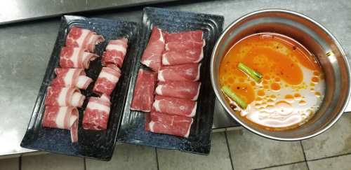 Two plates of sliced meat next to a bowl of spicy broth with green onions, set on a kitchen countertop.