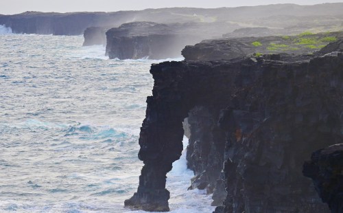 Rocky coastline with cliffs and waves crashing against the shore, shrouded in mist.