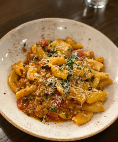 A bowl of pasta with meat sauce, topped with grated cheese and herbs, served on a wooden table.