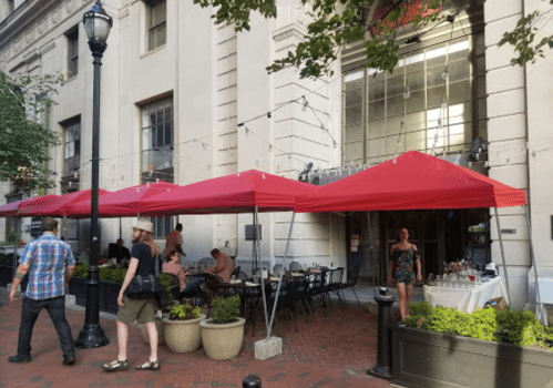 Outdoor dining area with red canopies, tables, and people enjoying their meals in a city setting.