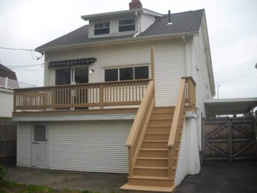 A two-story white house with a wooden deck and stairs leading to the entrance, set against a cloudy sky.