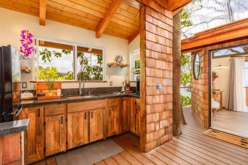 Cozy kitchen with wooden cabinets, large windows, and a view of greenery, featuring a modern stove and natural light.