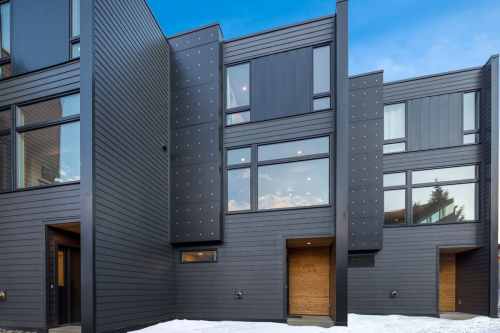 Modern black-clad buildings with large windows and wooden accents, set against a clear blue sky. Snow on the ground.