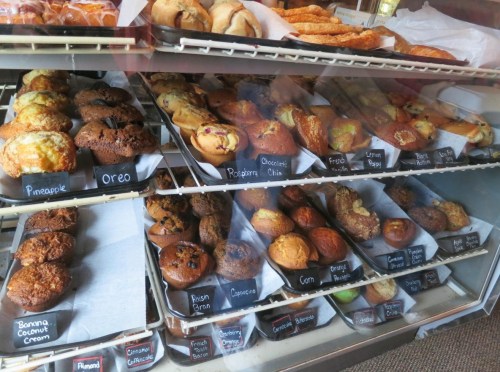 A display case filled with various baked goods, including muffins, pastries, and cookies, labeled with names.