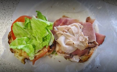 A sandwich with lettuce, tomato, and layers of sliced ham and turkey on a toasted bun.