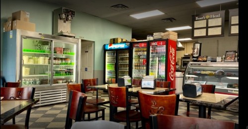 Interior of a casual dining area with tables, drink coolers, and a display case, featuring a checkered floor.