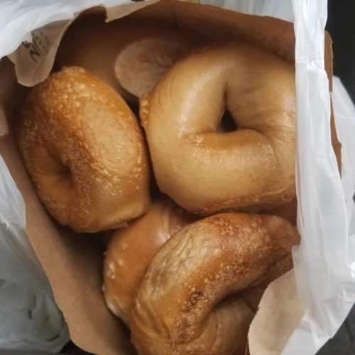 A bag filled with several golden-brown bagels, some with a shiny crust and a sprinkle of sesame seeds.
