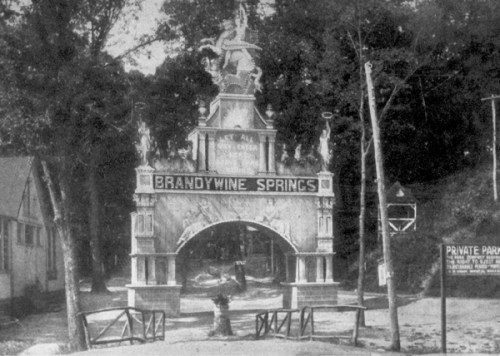 Historic entrance archway of Brandywine Springs, featuring ornate sculptures and signage, surrounded by trees.