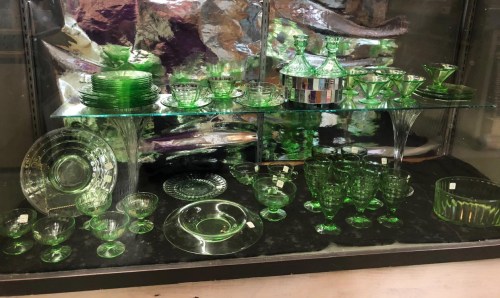 A display of various green glassware, including plates, bowls, and cups, arranged on glass shelves.