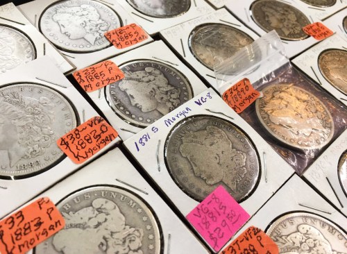A collection of coins displayed in holders, with price tags and a small bag containing a gold coin.