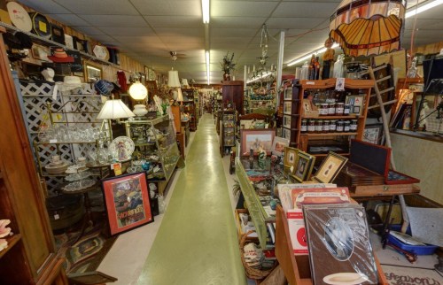 A narrow aisle in an antique store filled with various vintage items, furniture, and decor on both sides.
