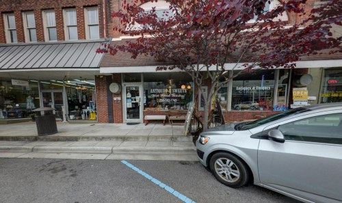 A storefront with a sign reading "Antiques & Swedes," featuring a tree and parked car in front.
