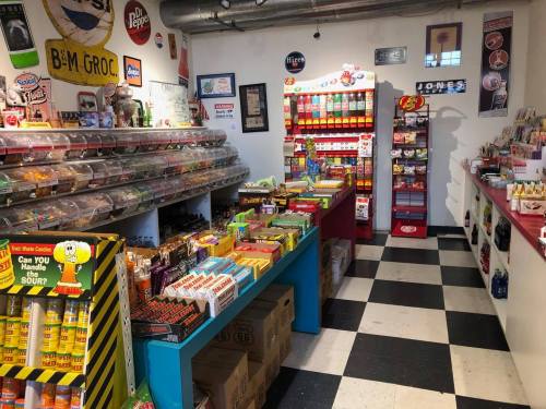 A colorful retro grocery store interior filled with candy, snacks, and vintage signage on the walls.