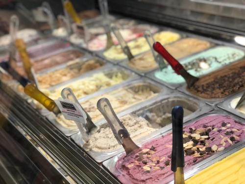 A variety of colorful gelato flavors displayed in metal containers with scoops and labels.