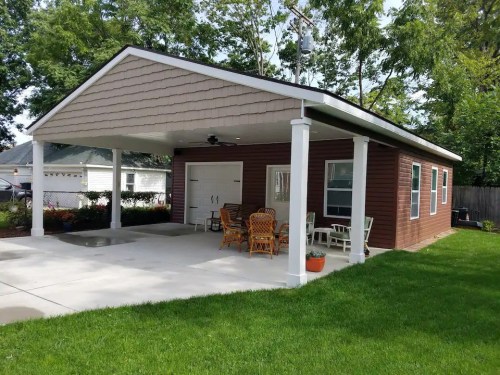 A modern brown house with a covered porch, white columns, and outdoor seating on a green lawn.