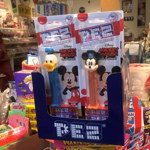 Two PEZ dispensers featuring Mickey Mouse and Donald Duck, displayed in a colorful candy shop.