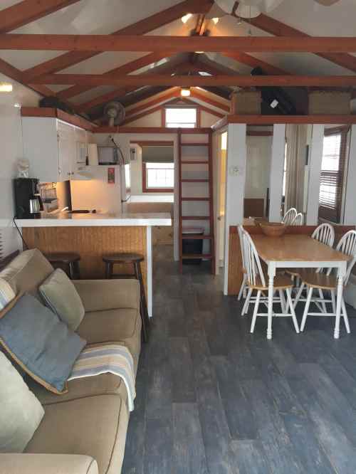 Cozy interior of a small cabin featuring a living area, kitchen, dining table, and a staircase to a loft.