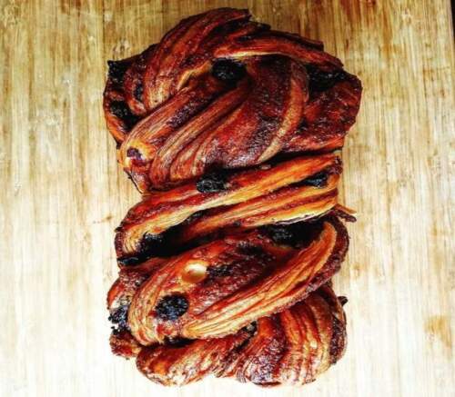 A beautifully braided pastry with a golden-brown crust and dark filling, resting on a wooden surface.