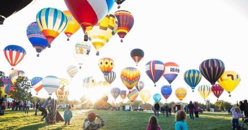 A vibrant scene of colorful hot air balloons in the sky, with spectators enjoying the festival on a sunny day.