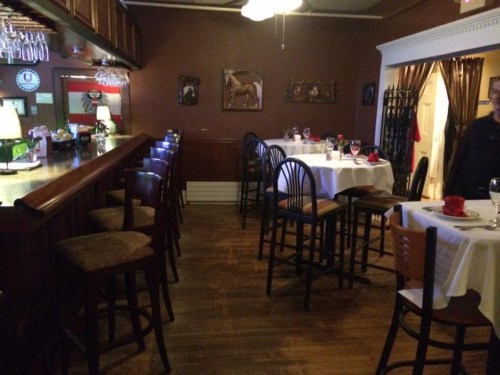A cozy restaurant interior with a bar, tables set for dining, and warm lighting.