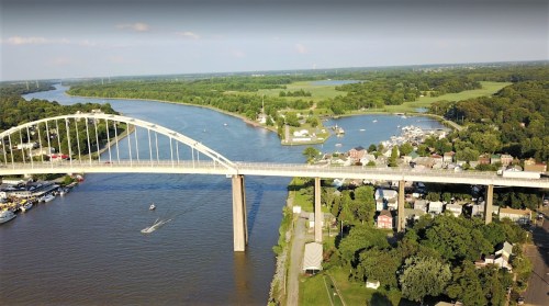 Aerial view of a river with a bridge, boats, and lush greenery along the banks.