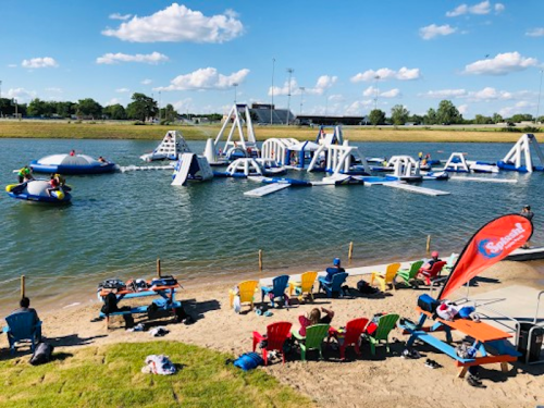 A vibrant water park scene with inflatable structures, people enjoying the water, and colorful beach chairs on the shore.