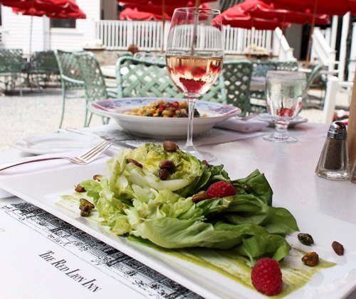 A fresh salad with lettuce, raspberries, and nuts, accompanied by a glass of white wine on a restaurant table.