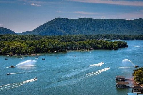 A scenic view of a lake surrounded by mountains, with boats and water sprays creating a lively atmosphere.