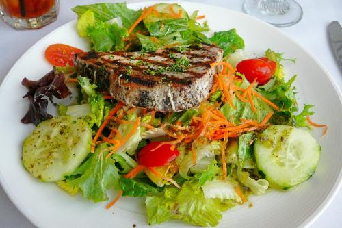 A fresh salad topped with grilled tuna, cherry tomatoes, cucumbers, and shredded carrots on a white plate.