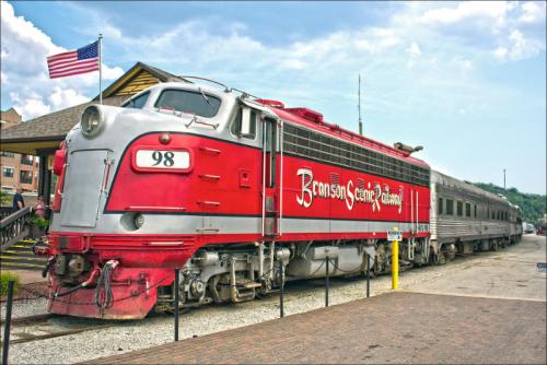 A vintage red and silver train at a station, with an American flag in the background and a passenger car attached.