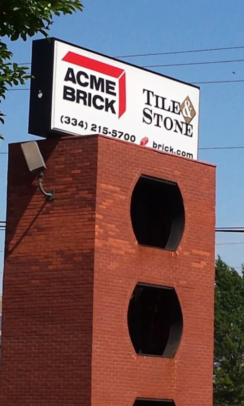 Sign for Acme Brick Tile & Stone, featuring a brick building structure and clear blue sky in the background.