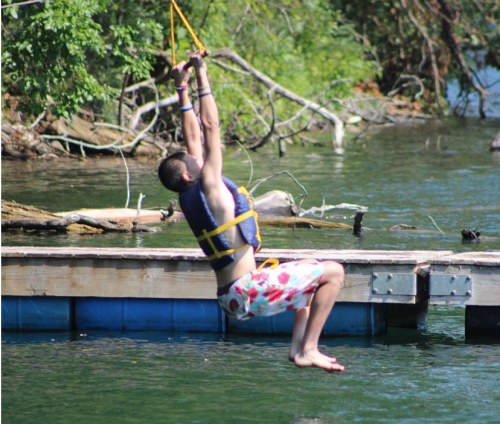 A person in swimwear swings from a rope over water, enjoying a summer day by the lake.