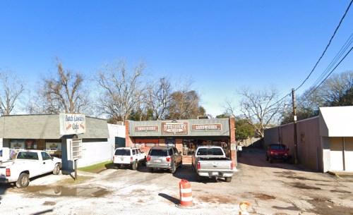 A small commercial area with several parked trucks and a restaurant, surrounded by trees and clear blue sky.