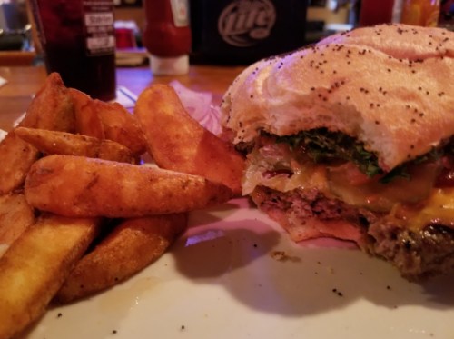 A close-up of a cheeseburger with lettuce and tomato, served with crispy potato wedges on the side.