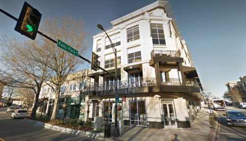 A modern multi-story building at an intersection, featuring a balcony and street signs for Falls Park.