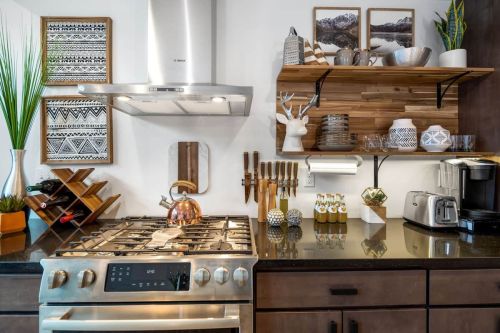 Modern kitchen with a gas stove, copper kettle, wooden shelves, and decorative items, featuring a stylish and organized layout.