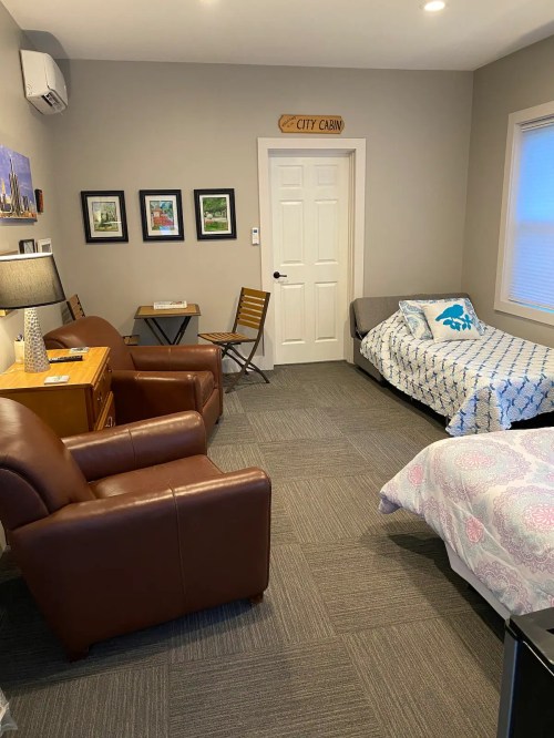 Cozy room with two armchairs, a bed, a small table, and wall art, featuring a door labeled "City Cabin."