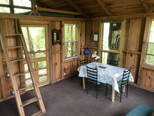 Cozy wooden interior of a treehouse with a dining table, chairs, and a staircase leading to a loft.